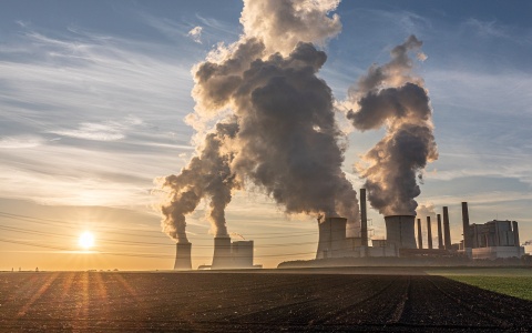 Das Bild zeigt ein Kohlekraftwerk, aus dessen Schornsteinen dunkler rauch aufsteigt
