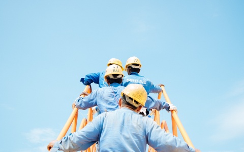 Das Bild zeigt Bauarbeiter und Bauarbeiterinnen die auf einer Leiter stehen von hinten
