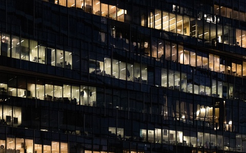 Bürogebäude in der Nacht mit beleuchteten Büros als Symbolbild für unbezahlte Überstunden