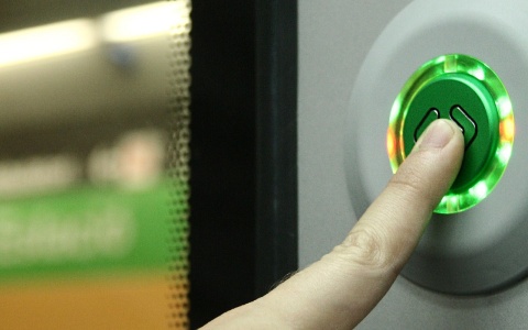 Das Bild zeigt einen Finger, der den Button einer automatischen Tür in einem Öffentlichen Verkehrsmittel drückt.