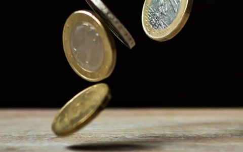Mehrere Euromünzen fallen auf einen Tisch. Der Hintergrund ist schwarz.