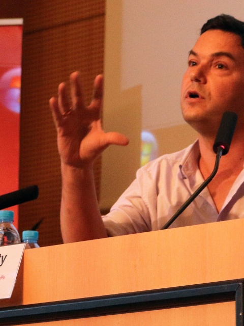 Thomas Piketty, vor sich ein Namensschild, gestikuliert beim Beantworten einer Frage.