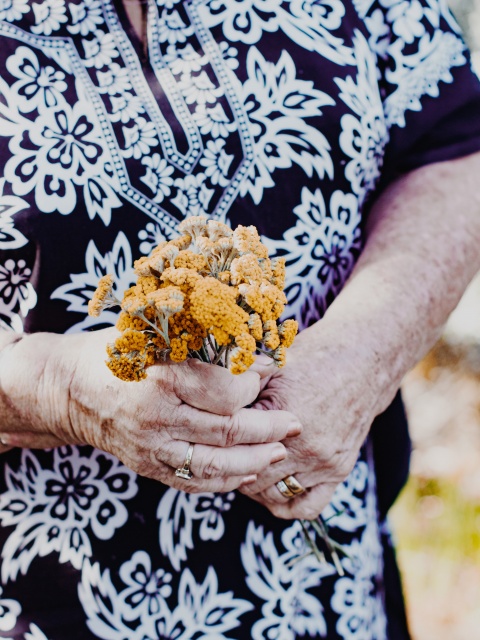 Eine Mindestpensionistin hält Wiesenblumen in der Hand. 