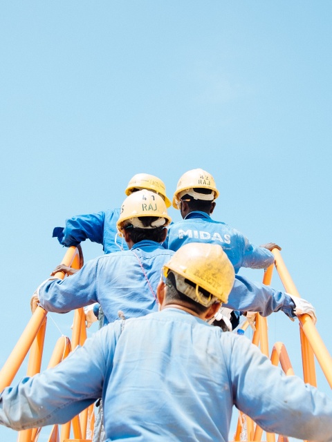 Das Bild zeigt Bauarbeiter und Bauarbeiterinnen die auf einer Leiter stehen von hinten